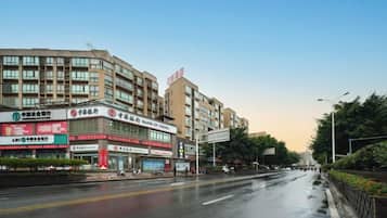 Un edificio de varios pisos con letreros comerciales, un camino mojado y un cielo despejado.
