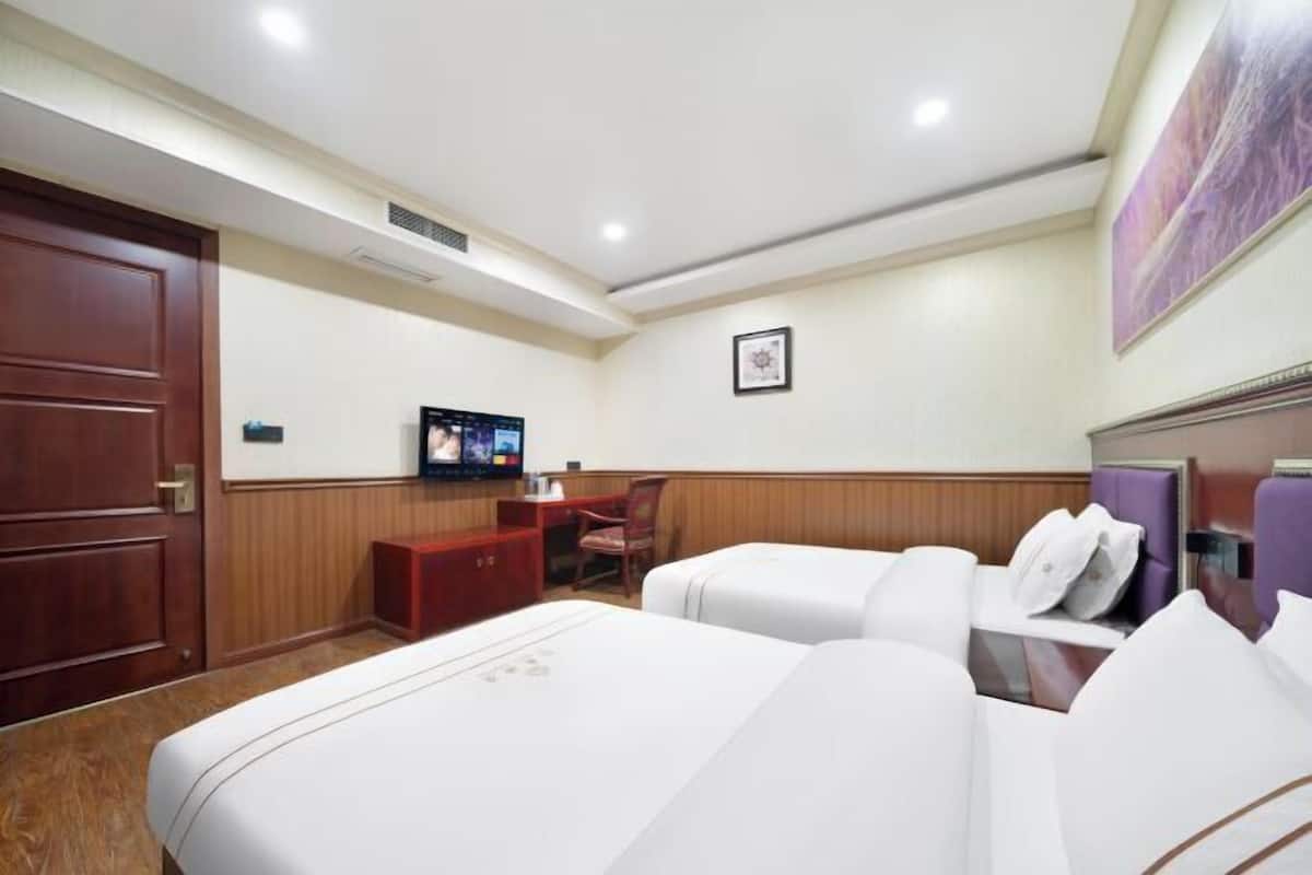 A hotel room with two beds, a desk, a television, and a framed picture on the wall.