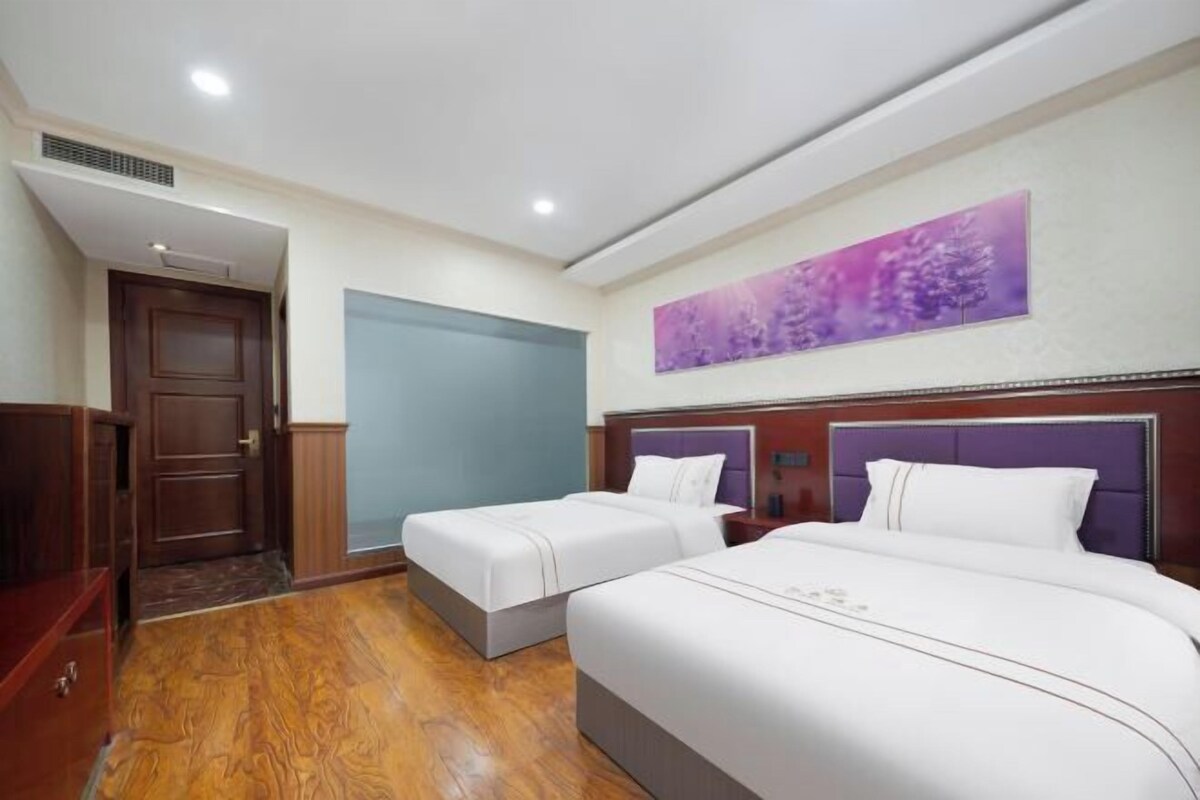 A hotel room with two beds, a wooden floor, a door, and a wall with a purple artwork.