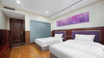 A hotel room with two beds, a wooden floor, a door, and a wall with a purple artwork.