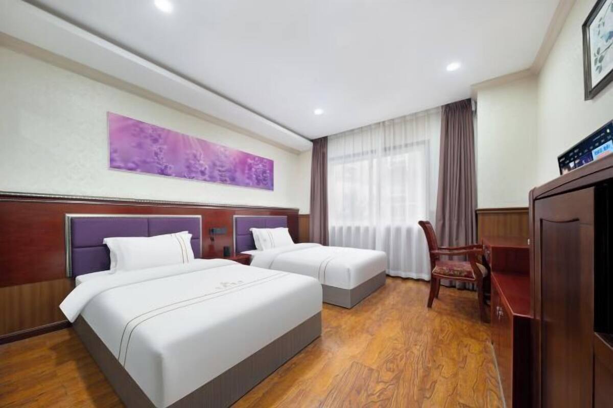 A hotel room with two beds, a desk, a chair, a television, and a painting on the wall.