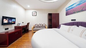 Un dormitorio con cama, escritorio, silla, televisor y un cuadro en la pared.
