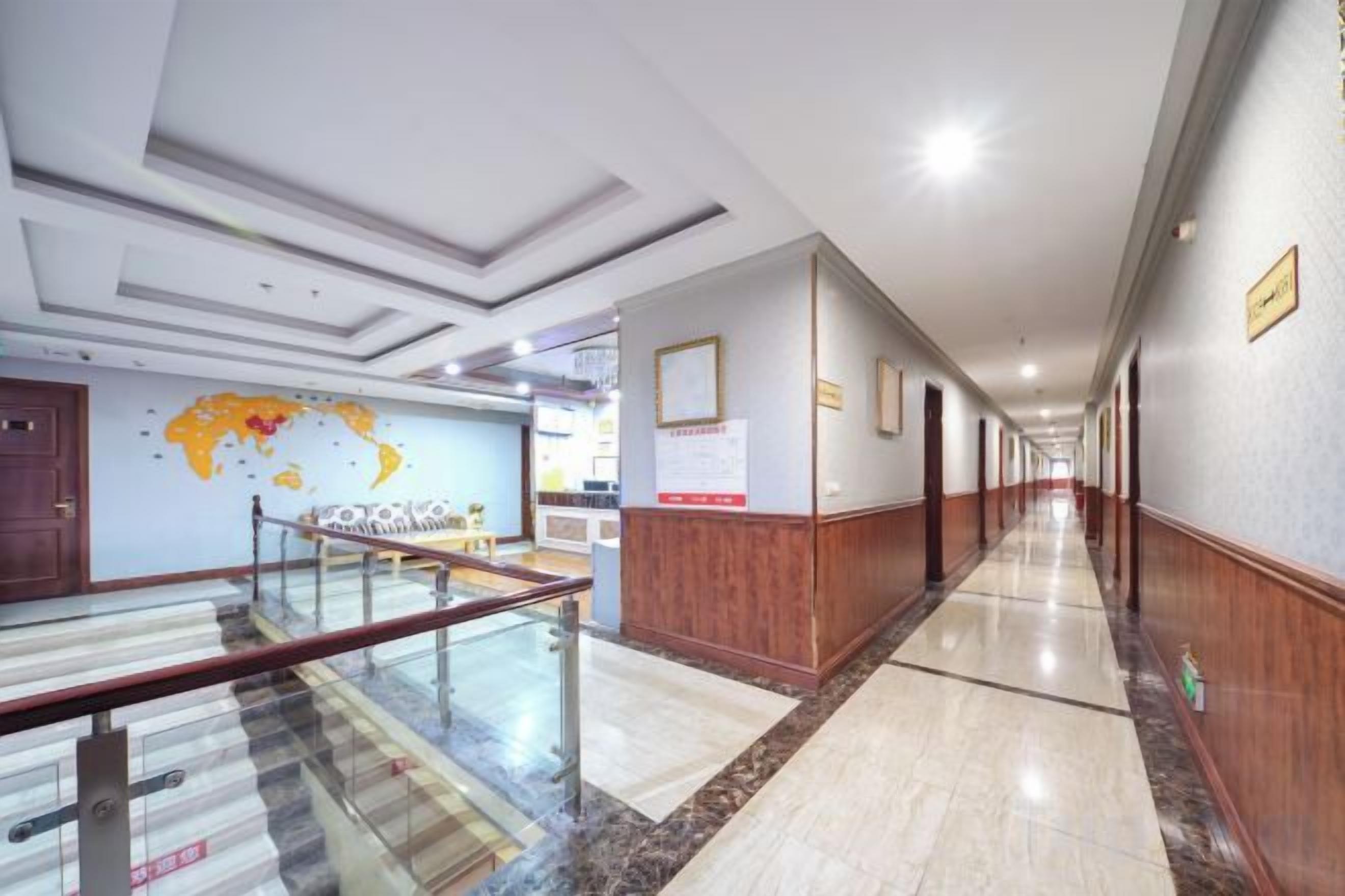 Un pasillo de hotel con suelo de mármol, paneles de madera, barandilla de vidrio y un mapa mundial en la pared.