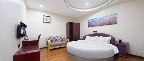 A bedroom with a round bed, a sofa, a TV, and a painting on the wall.