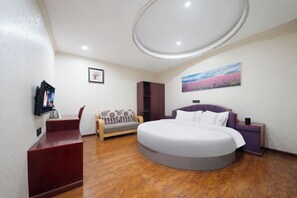 A bedroom with a round bed, a sofa, a TV, and a painting on the wall.