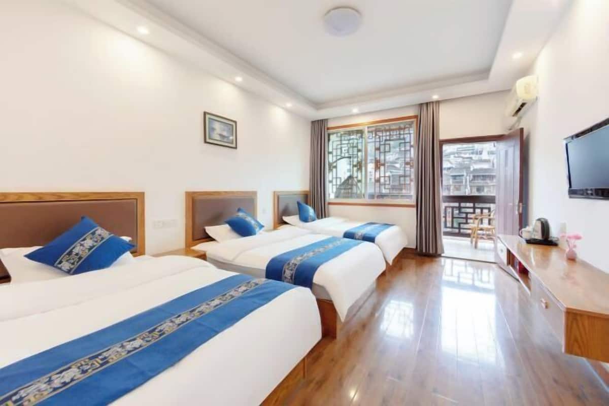 A hotel room with three beds, a TV, and a view of the city through the window.