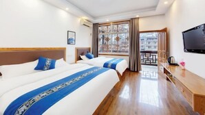 Camera d'albergo con due letti, una televisione, una scrivania in legno e vista su un edificio dalla finestra.