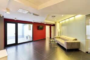 Un moderno vestíbulo de hotel con una pared de acento roja, un sofá, una mesa de centro de vidrio y un televisor de pantalla plana montado en la pared.