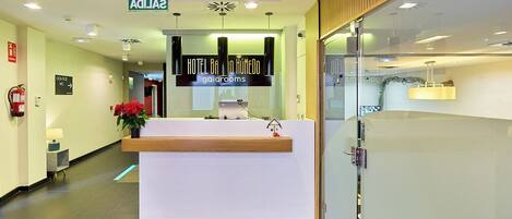 A hotel reception area with a modern design, including a reception desk, a sign for the hotel, and a fire extinguisher on the wall.