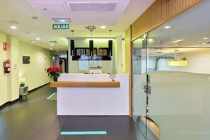 Ein Hotel-Empfangsbereich im modernen Stil, mit einer Rezeption, einem Hinweisschild des Hotels und einem Feuerlöscher an der Wand.