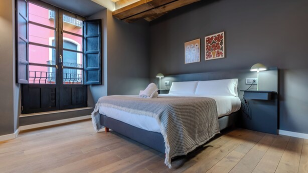 Un dormitorio con cama, lámparas de noche, una ventana con vistas y una pared decorada con obras de arte.