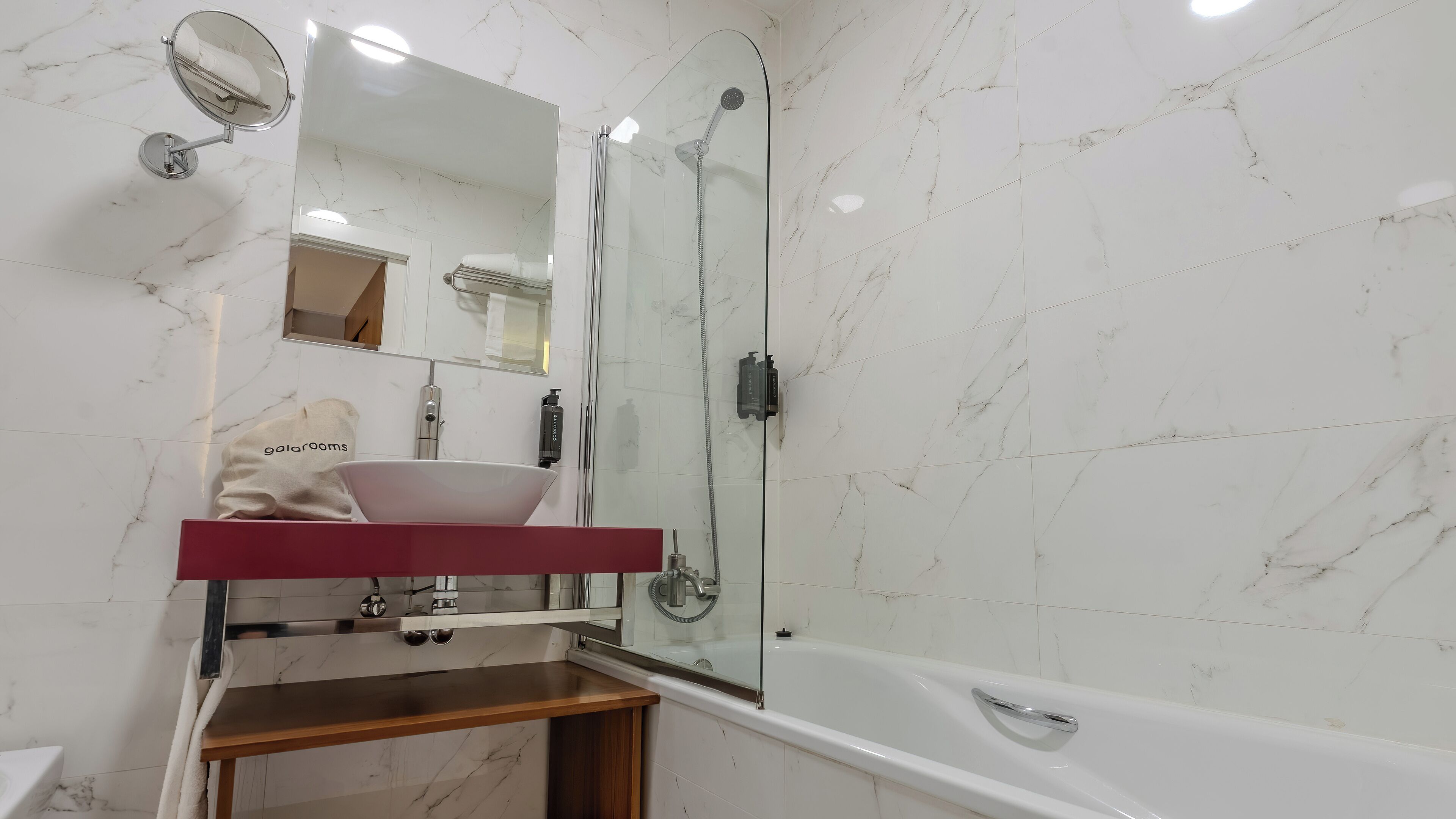 A bathroom with a marble-tiled wall, a glass-enclosed shower, a white bathtub, and a vanity with a mirror and sink.