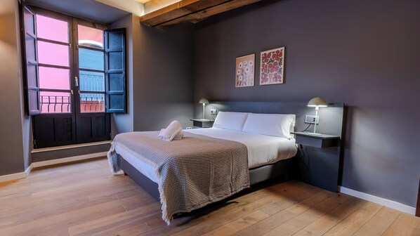 Un dormitorio con cama, mesitas de noche, una ventana con persianas y una obra de arte en la pared.
