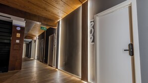 Un pasillo con piso de madera, una puerta blanca con cerradura electrónica y una señalización de salida de emergencia verde.