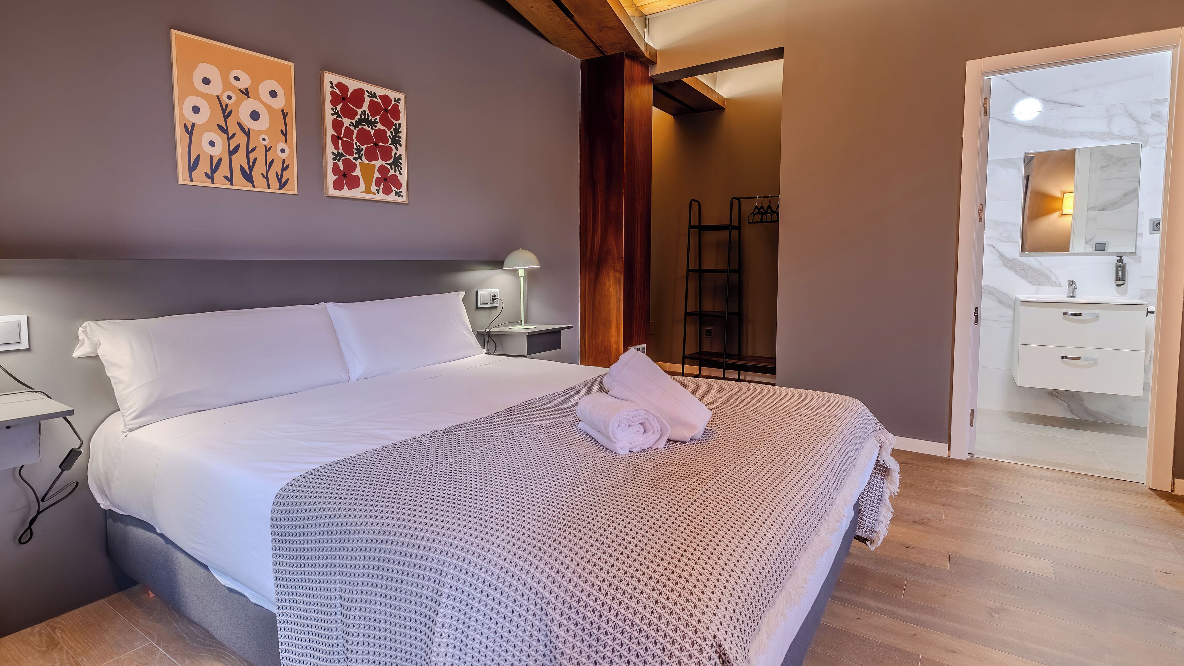 A neatly made bed with a rolled towel, a bedside lamp, and two wall art pieces.