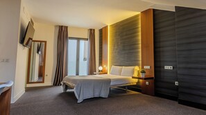 Una habitación de hotel moderna con cama, mesita de noche, lámpara y un espejo grande.