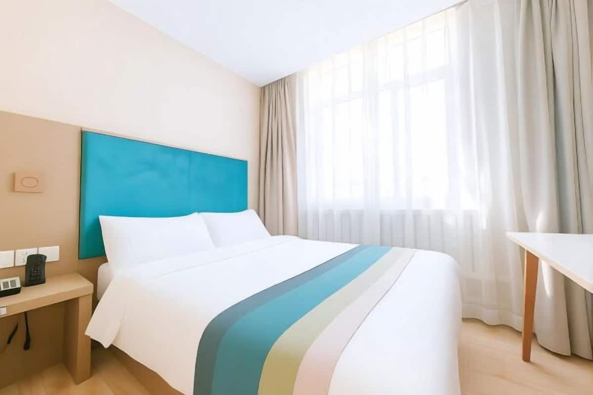 Una camera d'albergo con un letto, una scrivania, un telefono e una finestra con tende.
