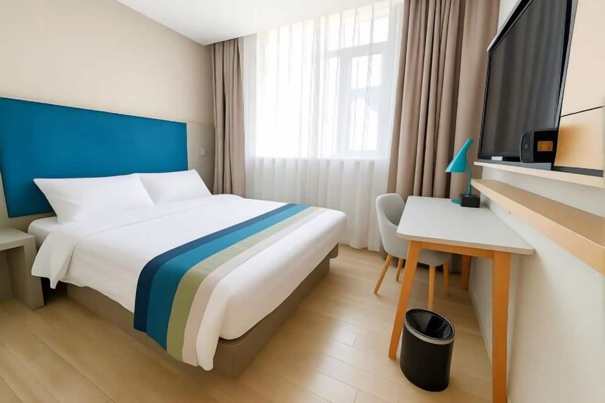 Una camera d'albergo con un letto, una scrivania, una sedia, una TV e una finestra con tende.