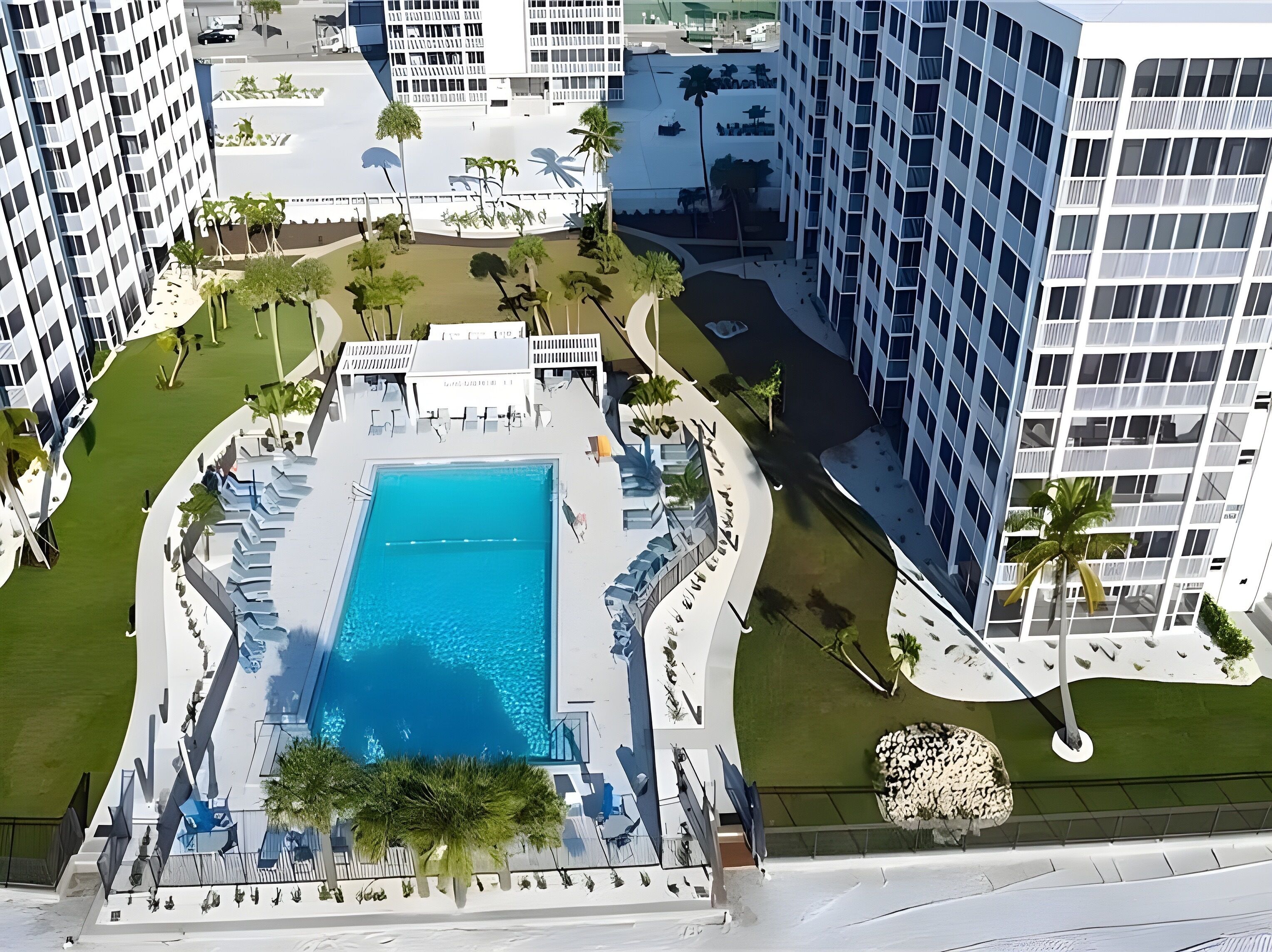 Ein Pool auf dem Dach, umgeben von Liegestühlen und Palmen, mit modernen Gebäuden im Hintergrund.