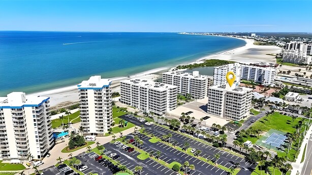 A high-rise hotel with multiple floors, a parking lot, and a beachfront view.