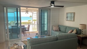 A living room with a green sofa, a small table with a candle, and a view of the beach through a sliding glass door.
