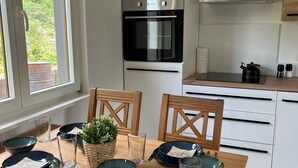 Una cocina moderna con horno empotrado, una mesa de comedor con platos, vasos y cubiertos, y sillas de madera.