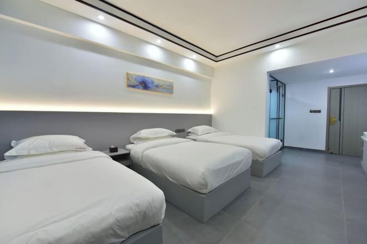 Een moderne hotelkamer met drie bedden op rij, een schilderij aan de muur en een deur naar een andere kamer.