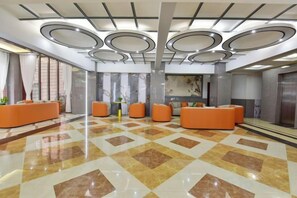 Una hall d'albergo con reception, area salotto e un grande specchio.