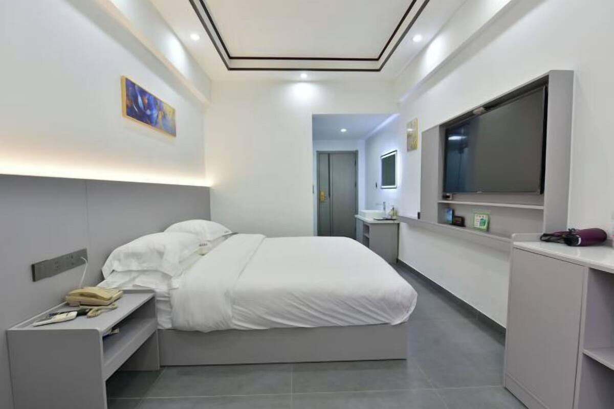 A modern hotel room with a bed, bedside table, and a TV mounted on the wall.