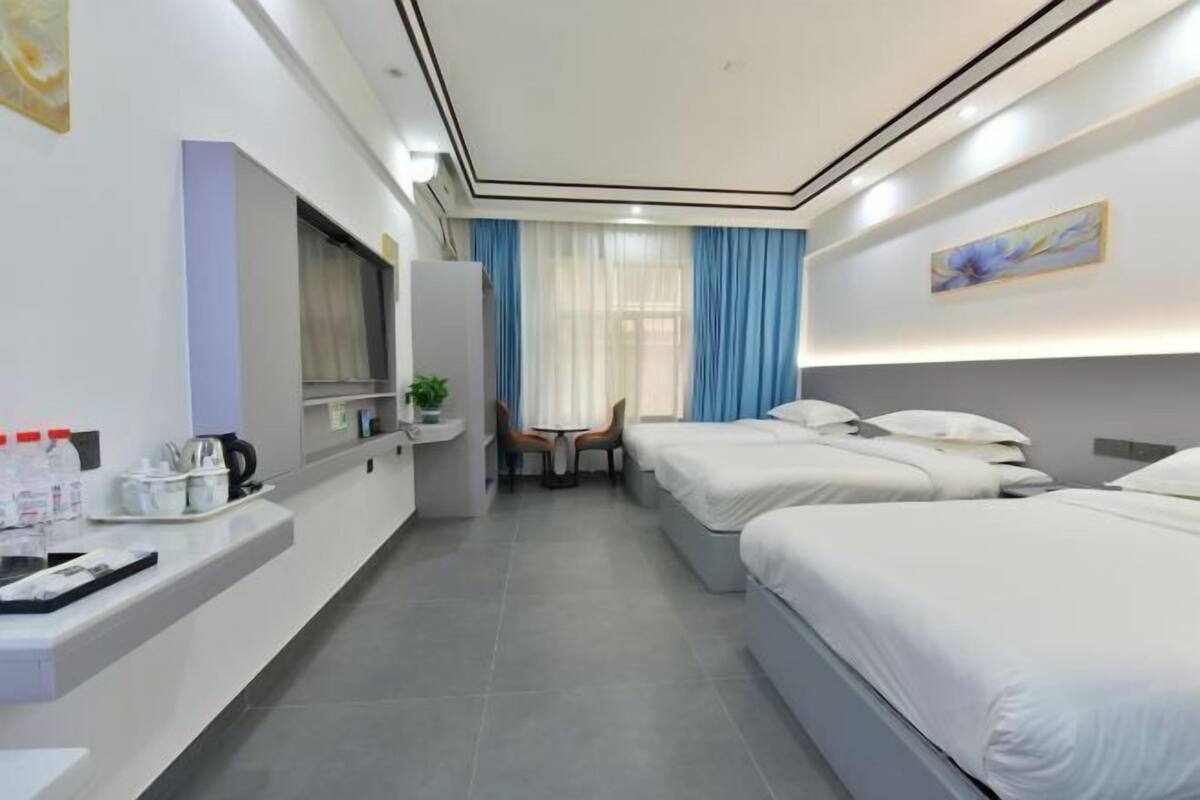 A hotel room with two beds, a desk, a chair, a small table, and a window with curtains.