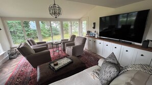A modern living room with a large TV, comfortable seating, and a view of the outdoors.