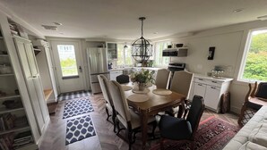 A modern kitchen with a dining area, featuring a large island, built-in appliances, and a view of greenery outside.