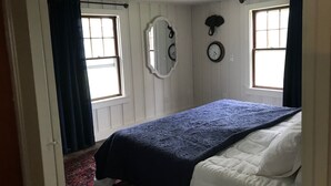 A bedroom with a bed, two windows with curtains, a ceiling fan, and two wall clocks.