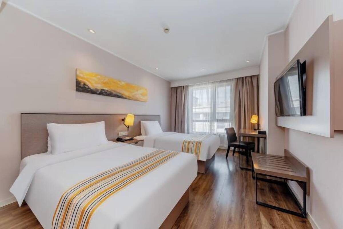 A hotel room with two beds, a desk, a TV, and a painting on the wall.