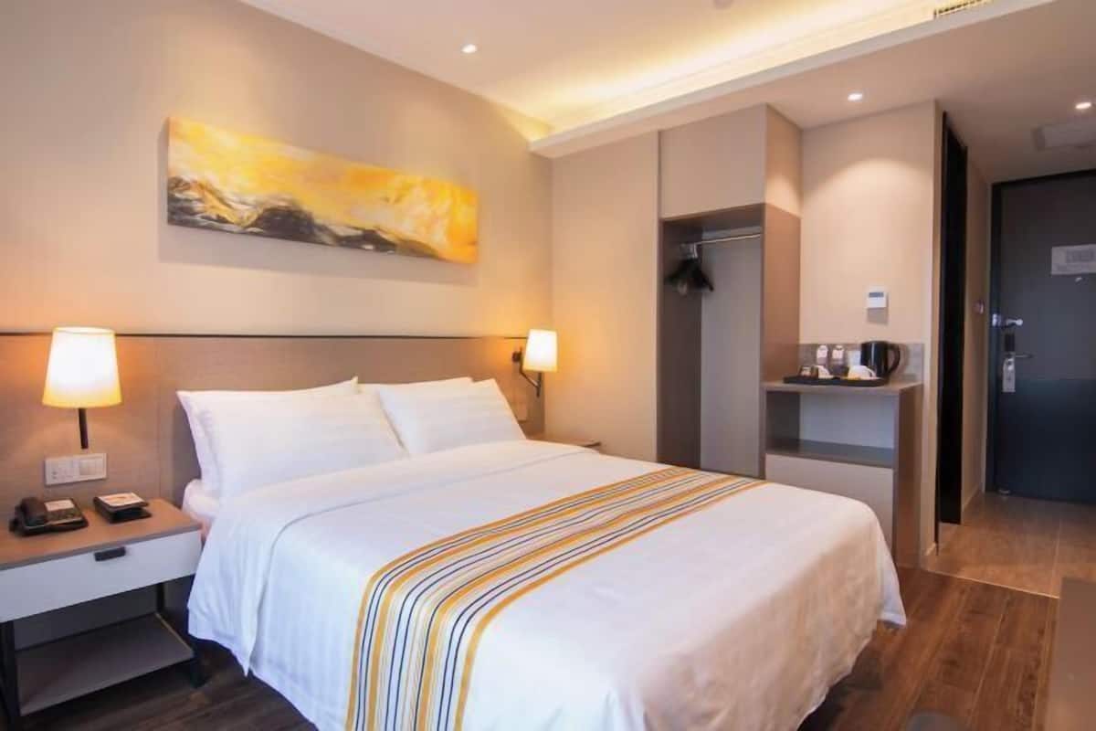 A hotel room with a bed, bedside lamps, a painting on the wall, a shower area, and a coffee machine.
