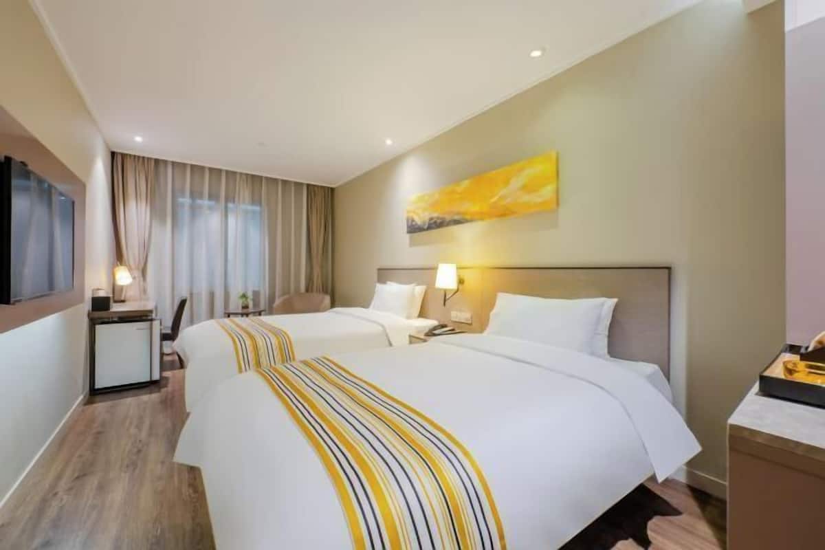 A hotel room with two beds, a desk, a chair, a TV, and a painting on the wall.