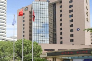 Ένα πολυώροφο κτίριο με μια μοντέρνα γυάλινη πρόσοψη, μια κατασκευή για την ανάρτηση σημαιών και μια επιγραφή με κινεζικούς χαρακτήρες.