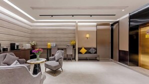 Un moderno vestíbulo de hotel con mostrador de recepción, zona de estar y una escalera que da a un ascensor.
