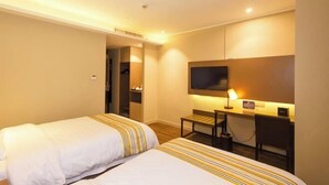 Habitación de hotel con dos camas, un escritorio, televisión y un pequeño rincón de descanso.