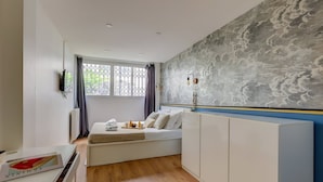 Une chambre d’hôtel moderne, équipée d’un lit, d’une armoire, d’un bureau avec un magazine, et ornée d’une grande fresque murale abstraite.