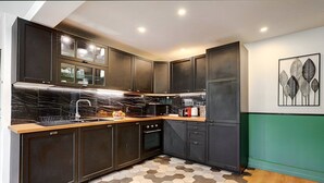Une cuisine moderne avec des meubles de couleur sombre, un pare-feu en marbre et un sol carrelé à motifs hexagonaux.