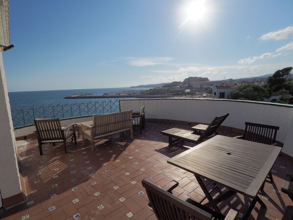 Een terras met uitzicht op zee, met een tafel, stoelen en een bankje.