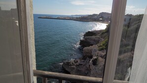 A coastal view from a window overlooking a rocky shoreline with a pier extending into the sea. - In front of the sea in Sitges (sitges)