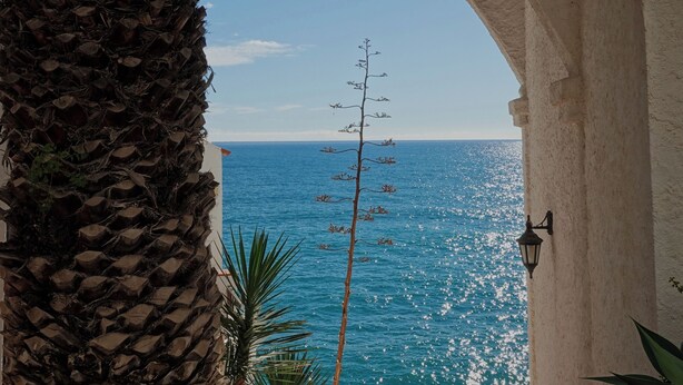 An arched doorway leading to a balcony overlooking a clear blue sea. - In front of the sea in Sitges (sitges)