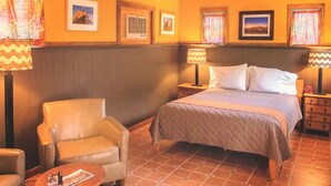 A hotel room with a bed, a chair, a nightstand, a lamp, and a small table.