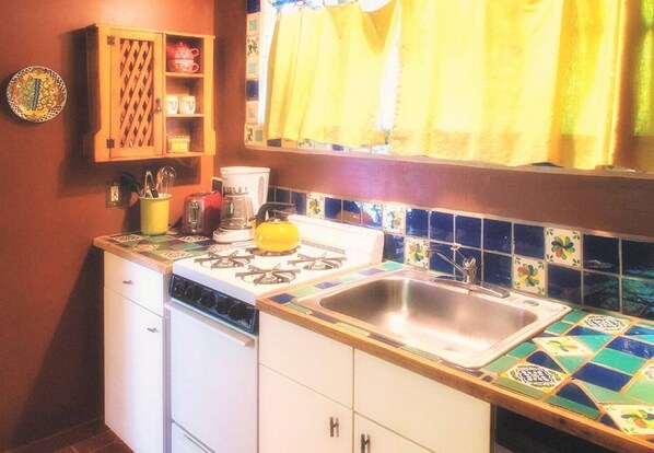 A compact kitchen with a gas stove, a sink, and a coffee maker.