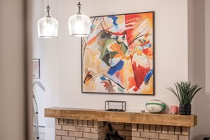 A room with a fireplace, a colorful abstract painting, and two hanging light fixtures.