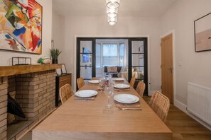 Ein Esszimmer mit Kamin aus Ziegelsteinen, einem langen Holztisch, gedeckt für sechs Personen, und einem großen abstrakten Gemälde darüber.