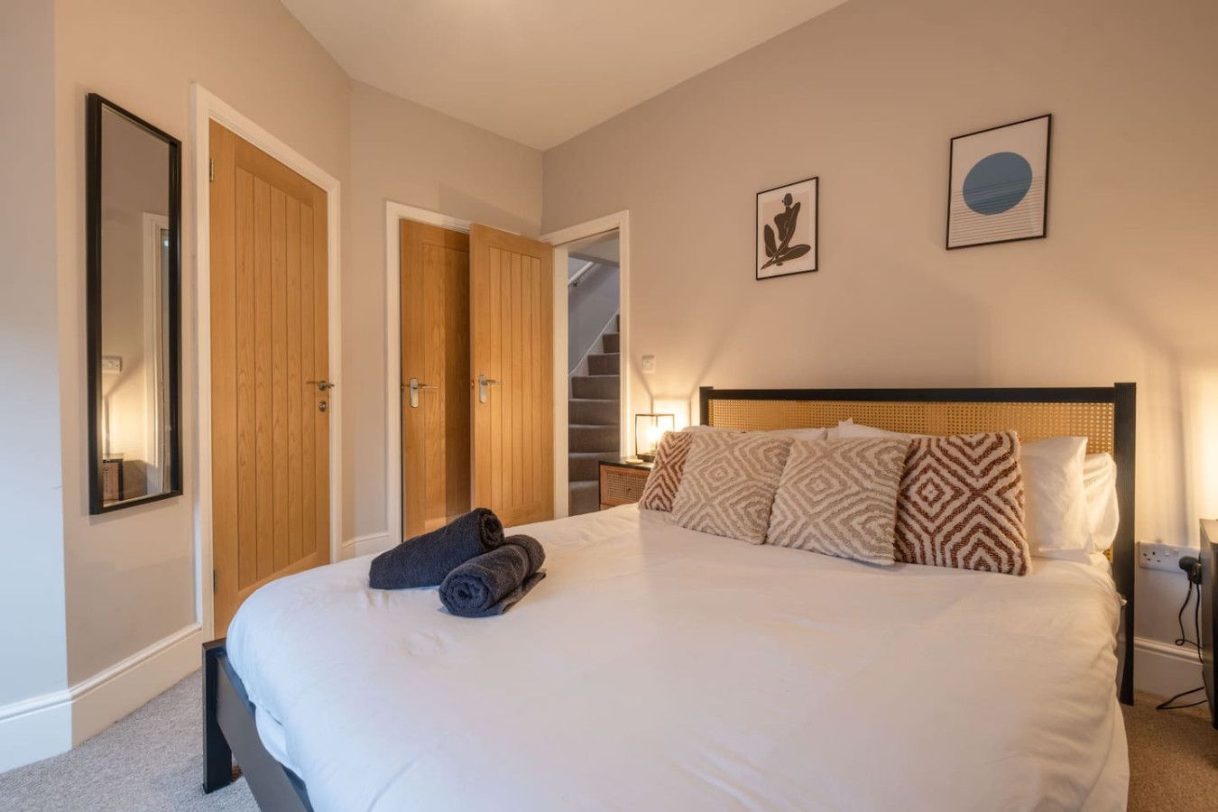 A bedroom with a large bed, a wooden wardrobe, a mirror, and two framed pictures on the wall.