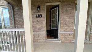 A brick house with a number '489' on the front wall, a covered porch with white railings, and a small front yard. - Clean precious house (Ajax)